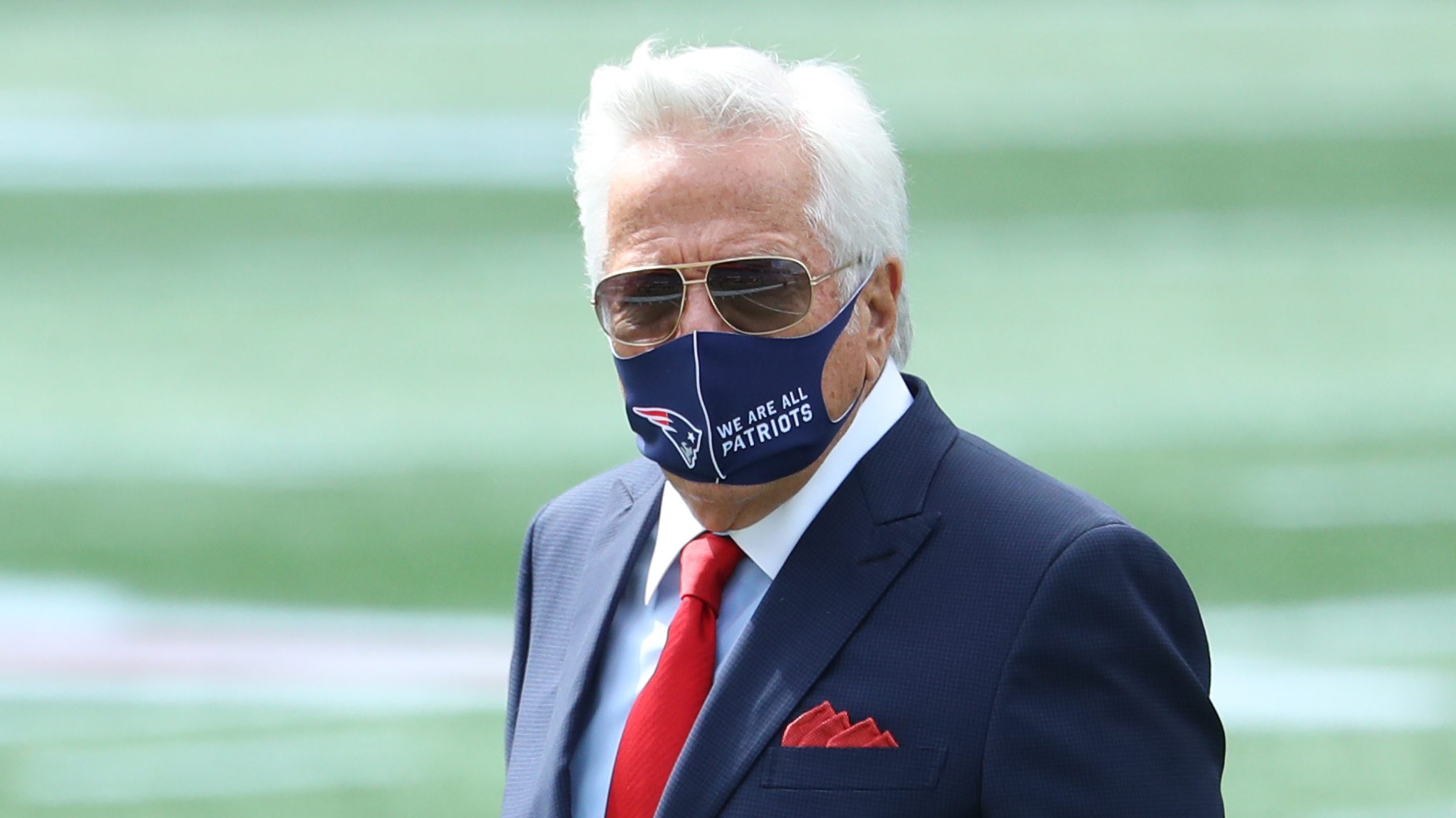 Patriots owner Robert Kraft wears a protective mask with "We Are All Patriots" stamped next to a Patriots logo.