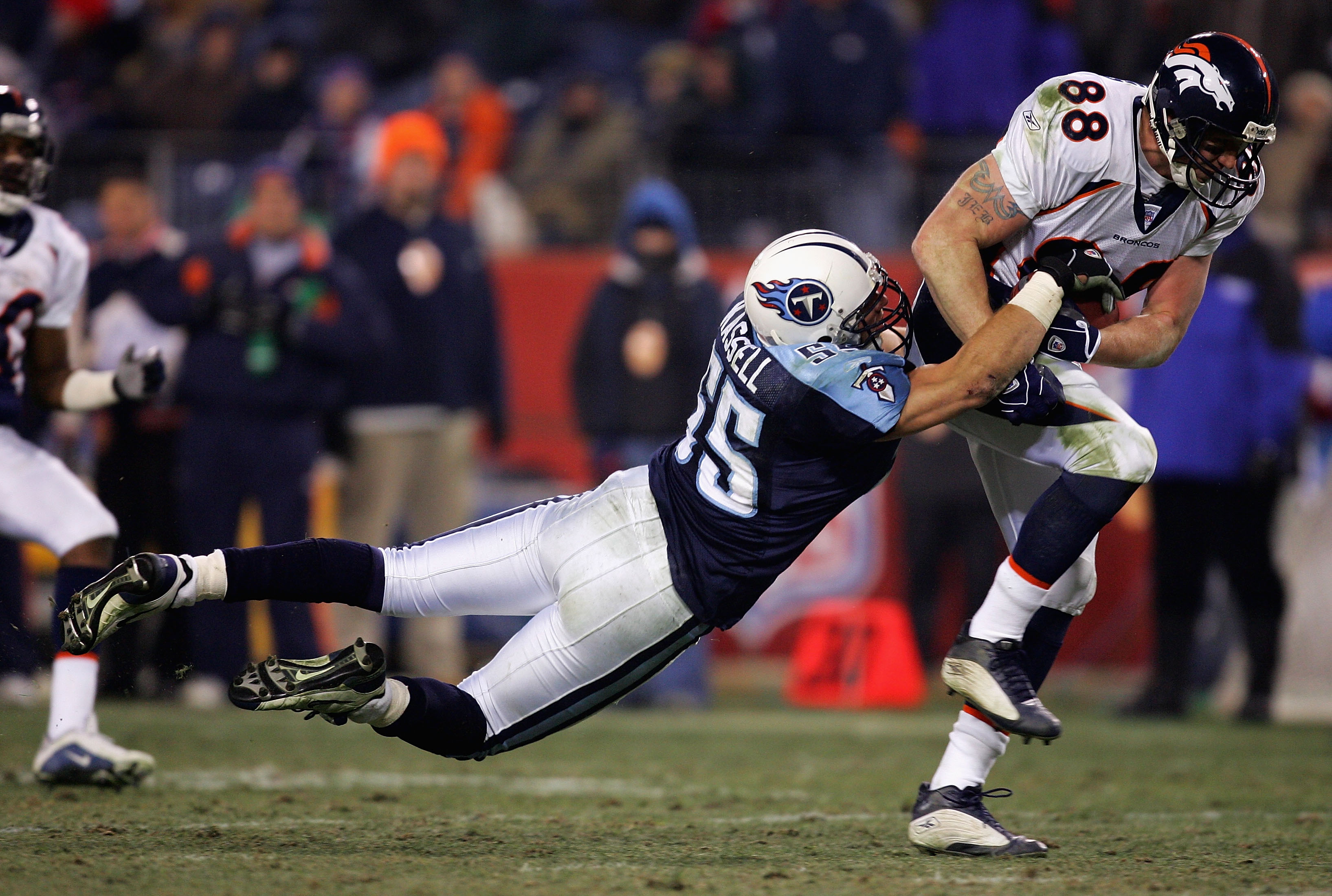 A player on the denver broncos grips the football at his hip while a player on the titans stretches airborn to try and strip it.
