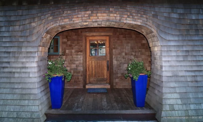 a wooden door with two blue planters on either side sits tucked inside a curved entryway