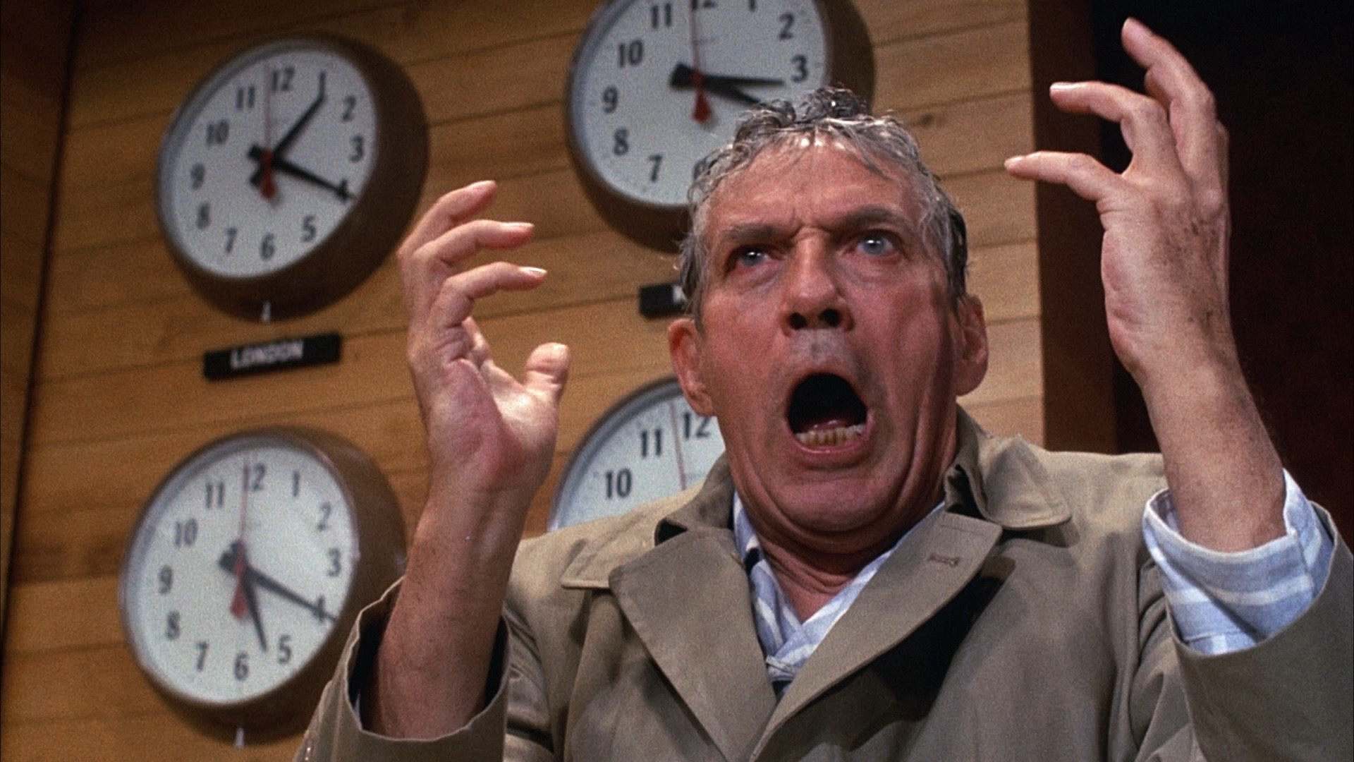 Howard Beale from the film Network, angry in front of clocks.