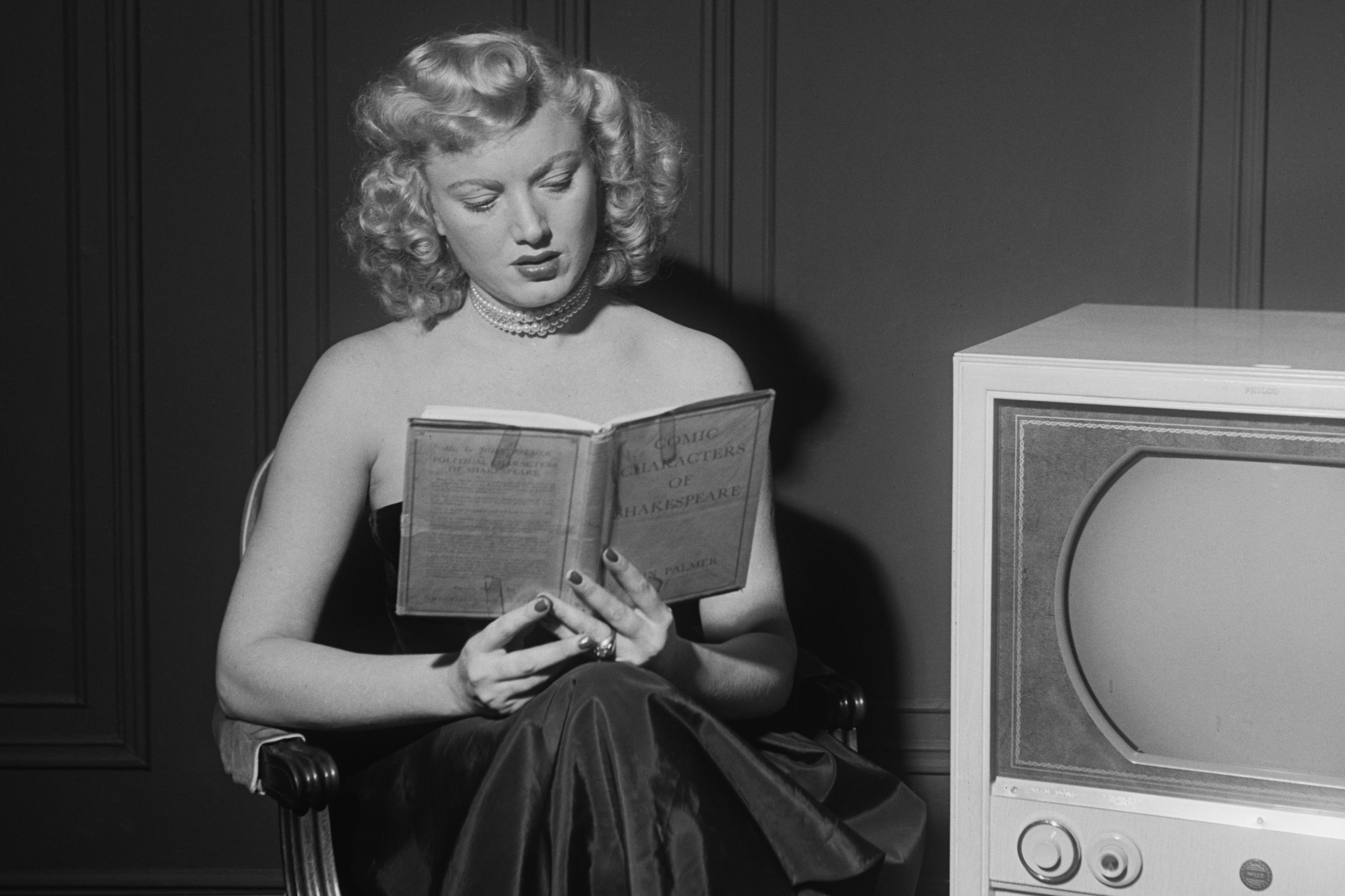 Actress Dagmar reads book beside TV in old black and white photo