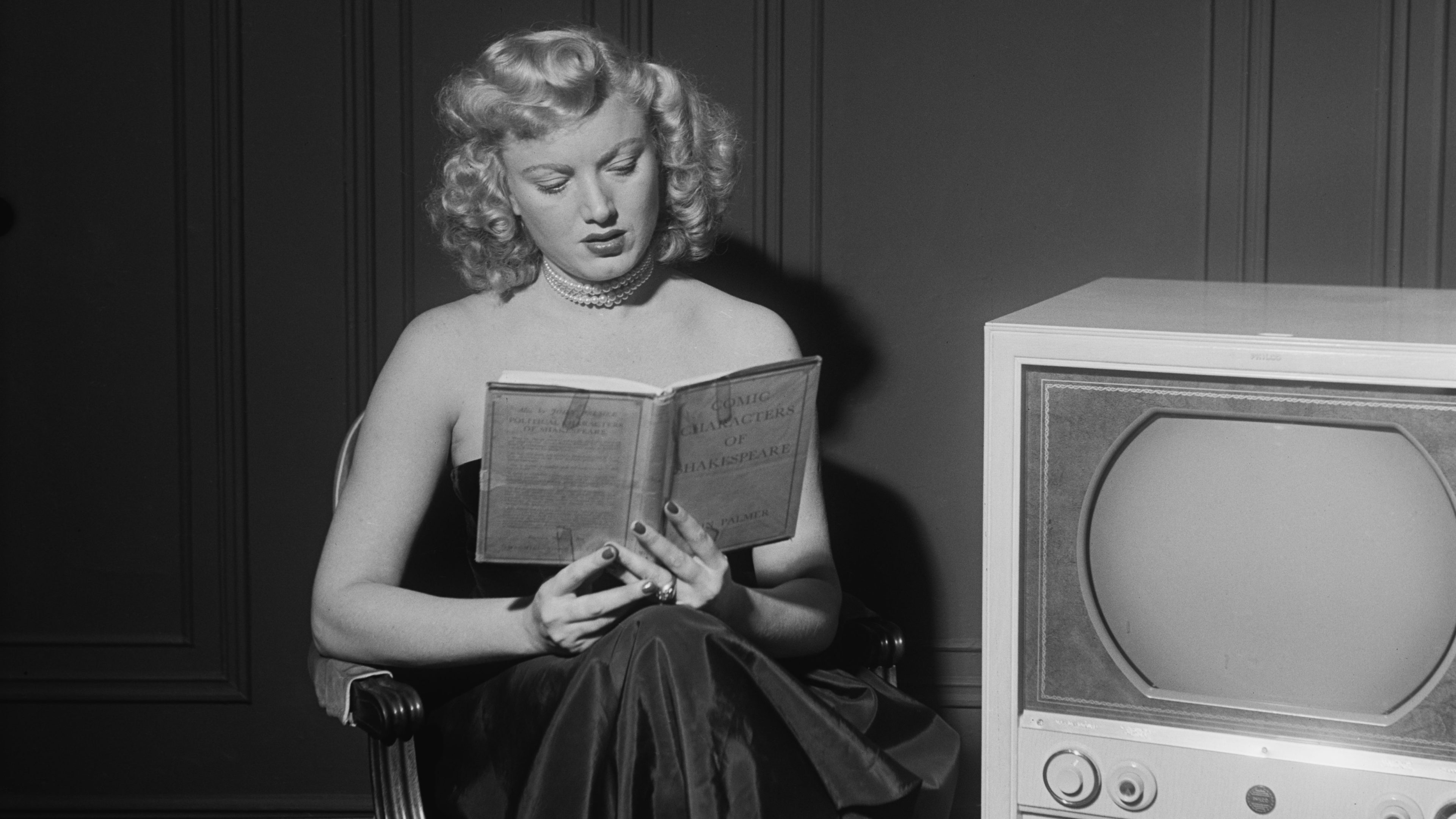 Actress Dagmar reads book beside TV in old black and white photo