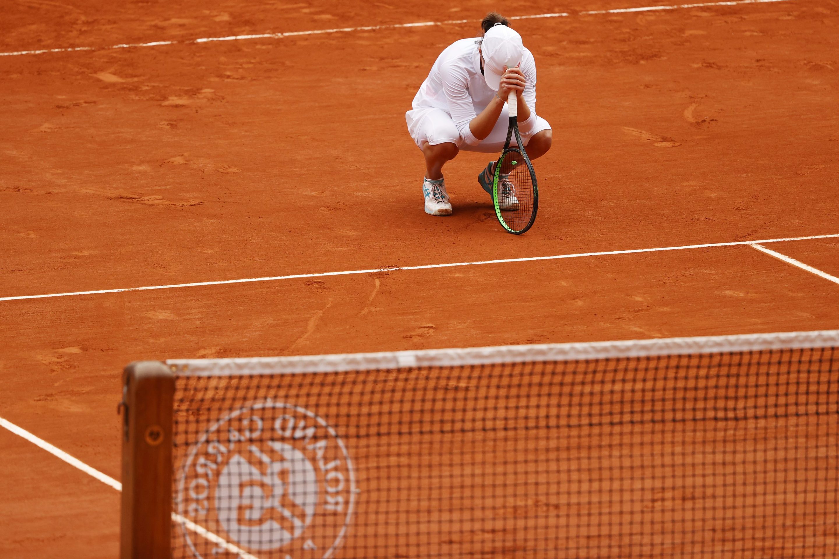 Iga Swiatek crouches to the court after winning the French Open.