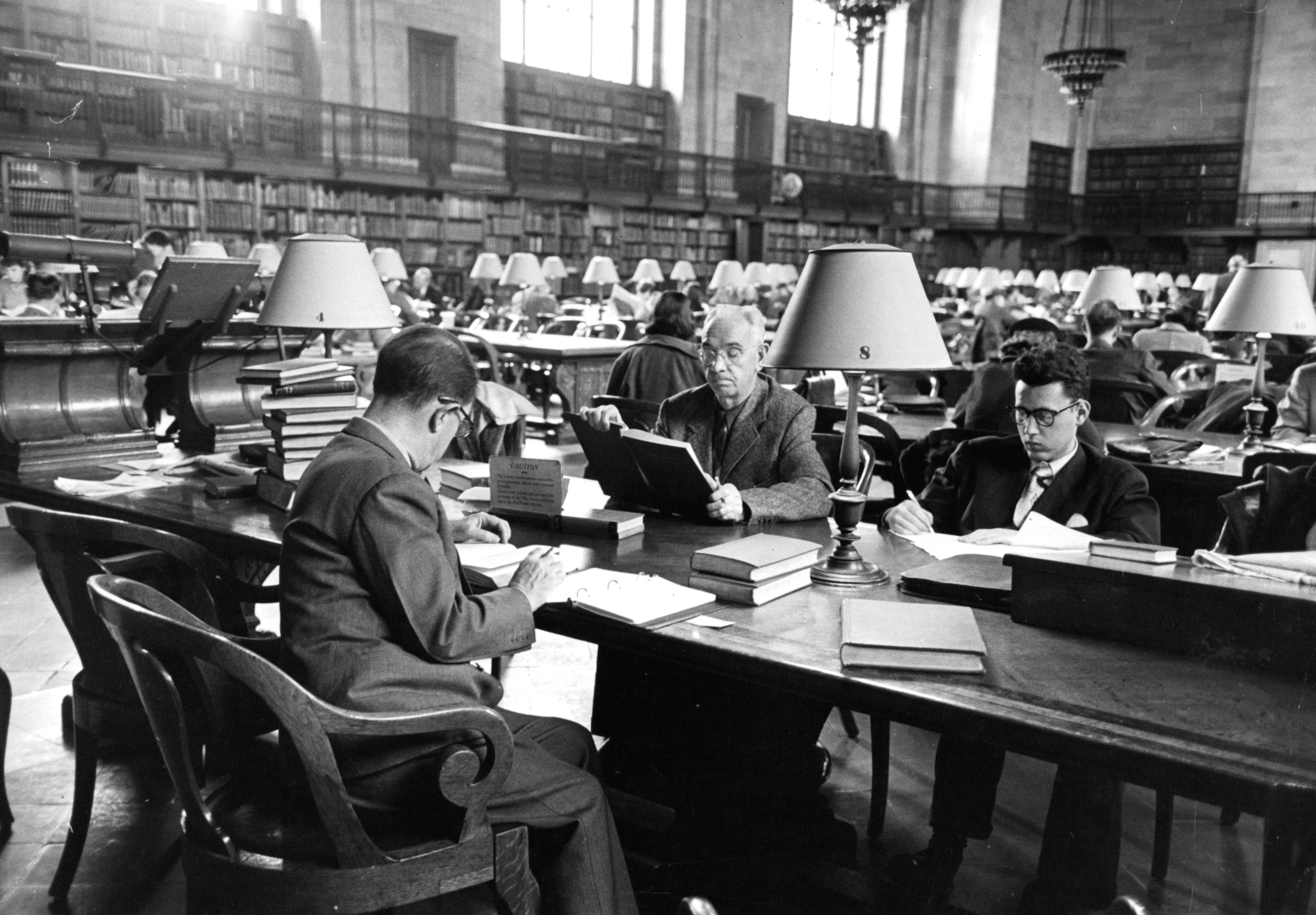 Three men share a table as they read in the South Reading Room at the main branch of the New York Public Library in New York City, New York, 1953.