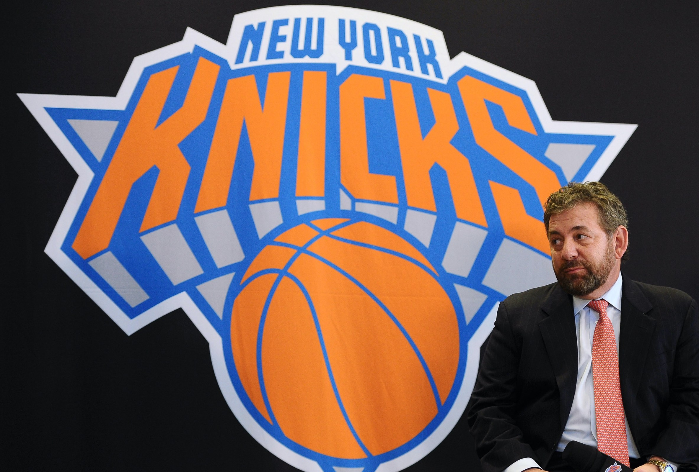 James Dolan sits next to a big Knicks logo.
