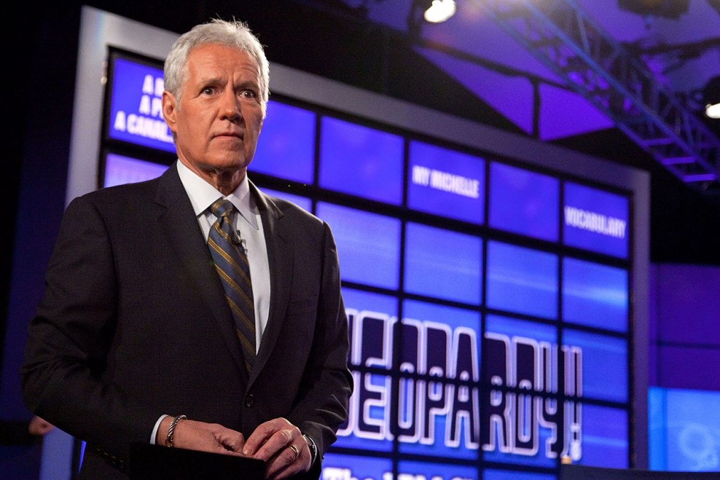 Alex Trebek stands in front of a Jeopardy! board