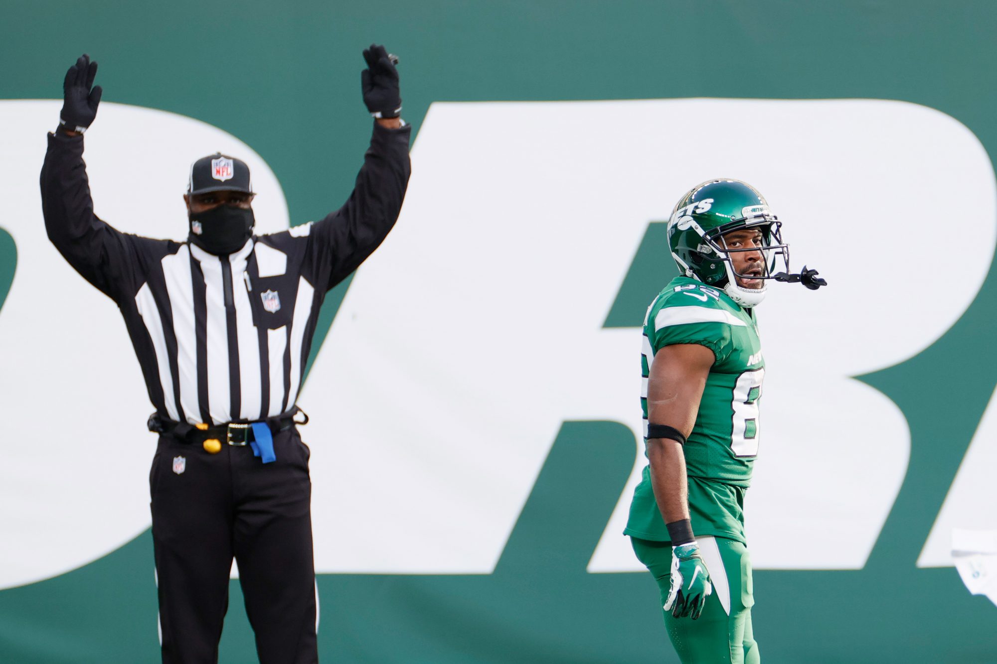 A referee signals "touchdown" behind a Jets player whose conflicted expression is inscrutable.