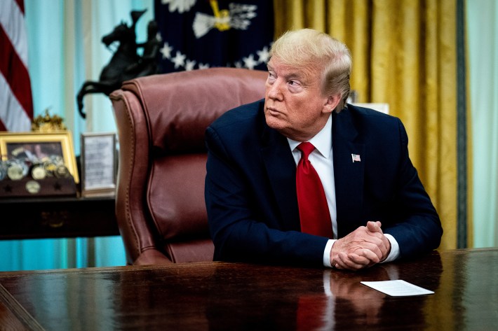 Donald Trump sitting at the presidential desk in a big red leather chair.