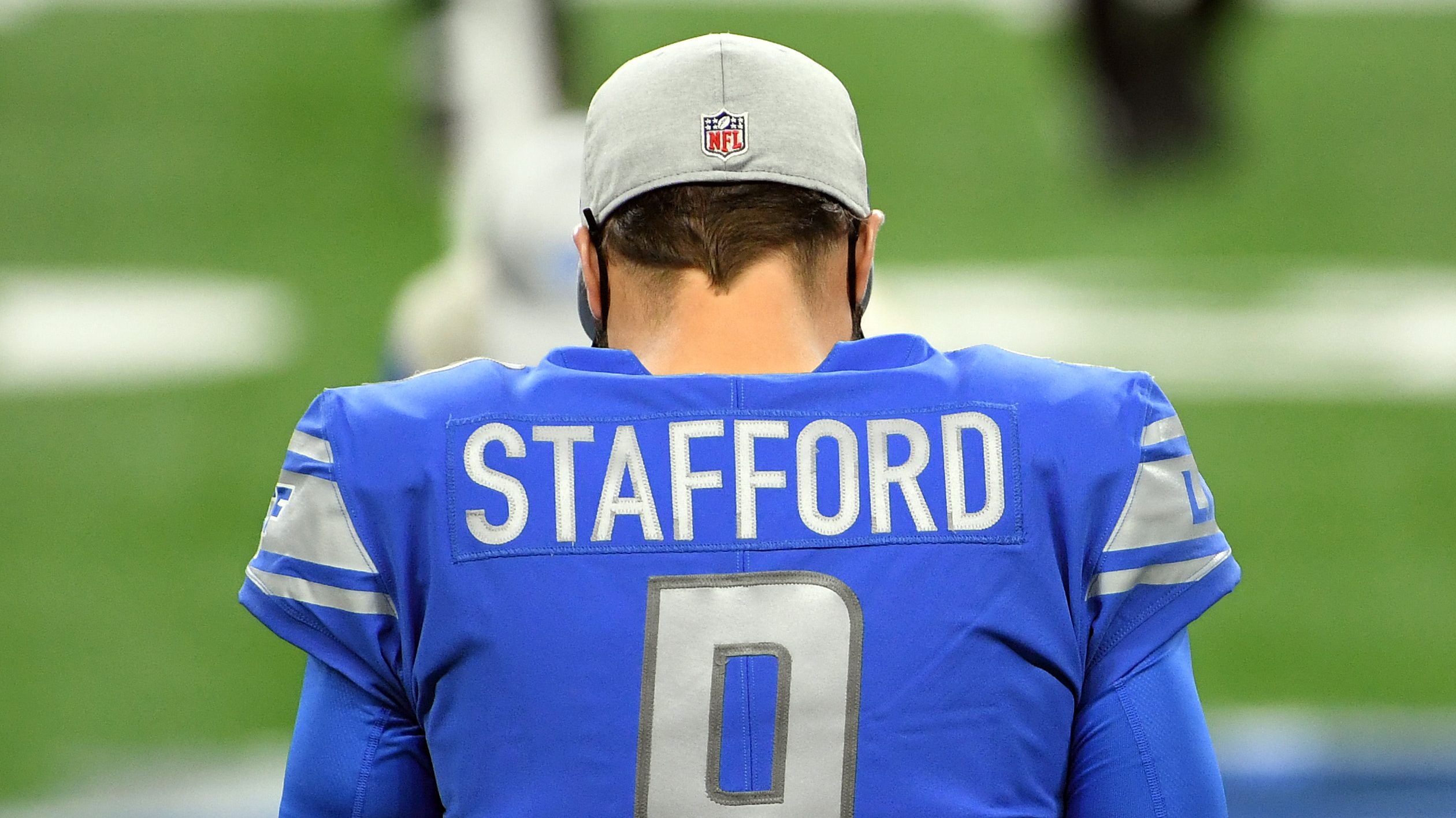 Matthew Stafford, quarterback of the Detroit Lions, stands on the field before the game against the Green Bay Packers at Ford Field on December 13, 2020 in Detroit, Michigan. Stafford has his back to the camera, all that's visible is his hat and his jersey.
