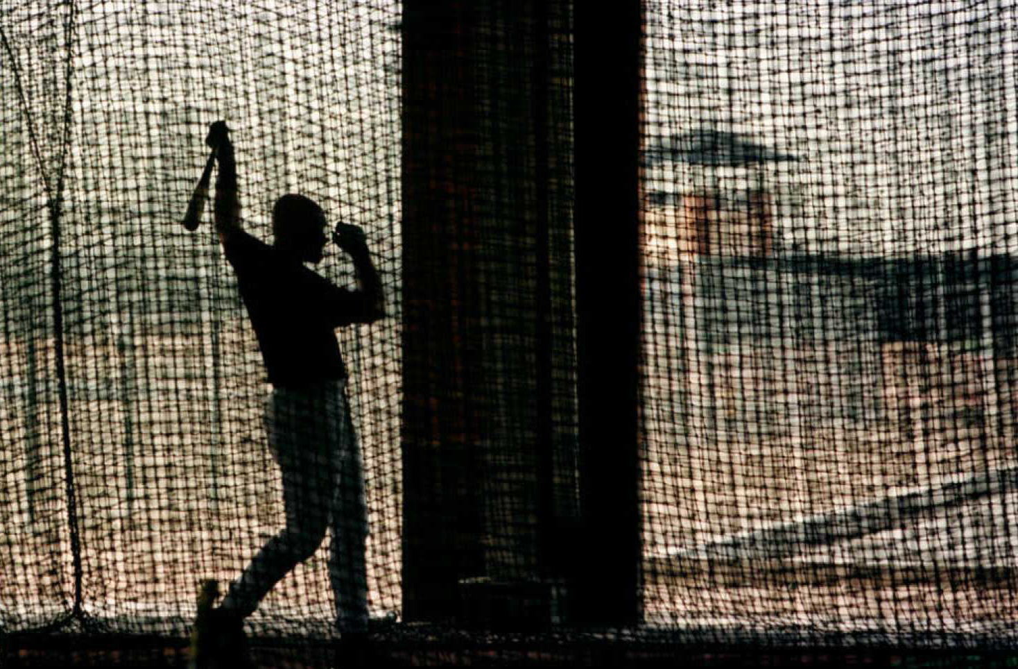 A baseball player is silhouetted as he follows through while practicing in the batting cages