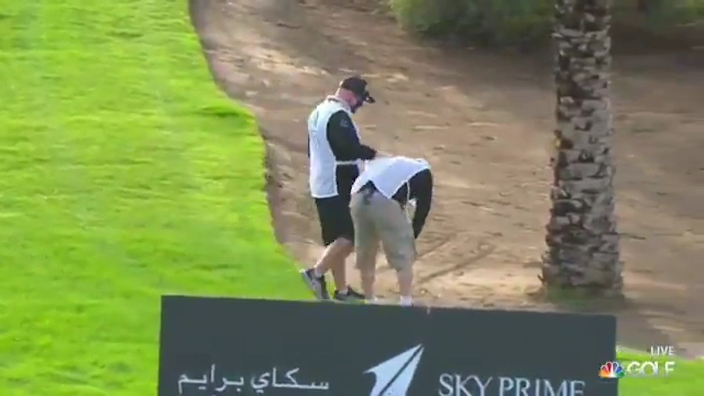 A volunteer at the Saudi International standing but bent over after being hit with a Dustin Johnson drive