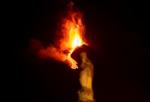 Etna erupting, with a statue out of focus in the foreground