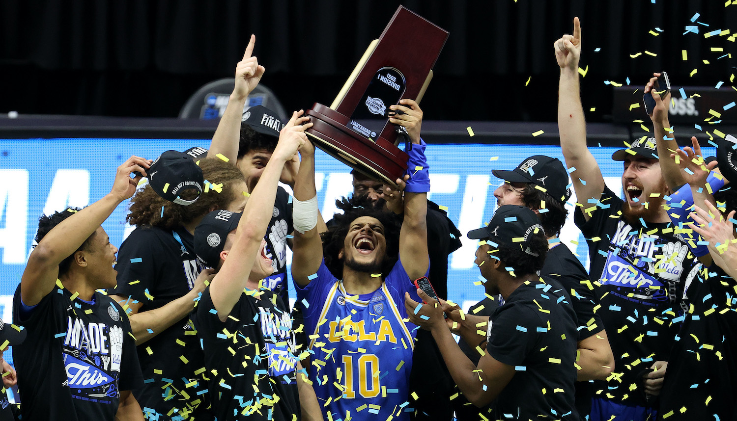 INDIANAPOLIS, INDIANA - MARCH 30: Tyger Campbell #10 of the UCLA Bruins celebrates with the East Regional Champion trophy after defeating the Michigan Wolverines 51-49 in the Elite Eight round game of the 2021 NCAA Men's Basketball Tournament at Lucas Oil Stadium on March 30, 2021 in Indianapolis, Indiana. (Photo by Andy Lyons/Getty Images)