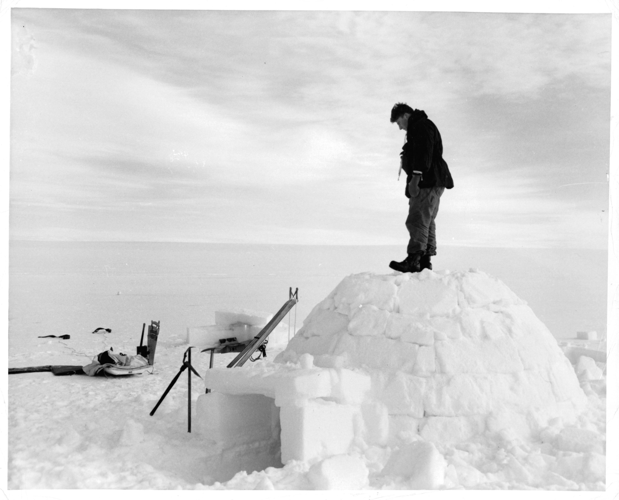 A man is standing on an igloo, in the near and far distance, there is snow for miles and miles in Greenland, 1953.