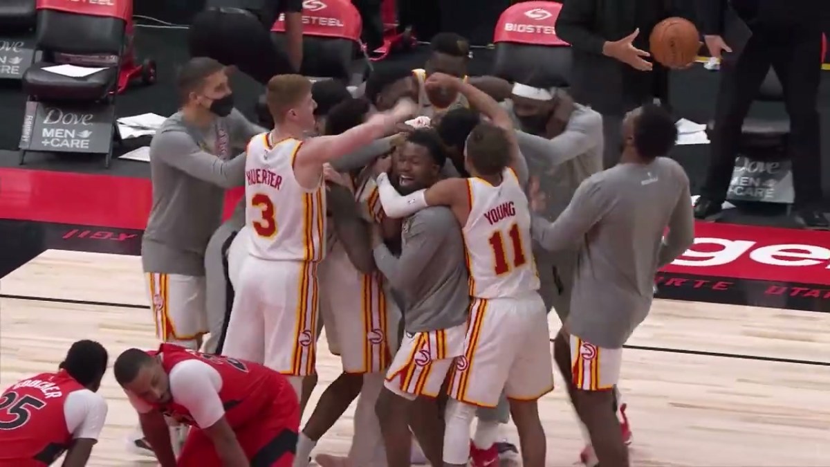 The Atlanta Hawks celebrate after a buzzer beater. They're all in a pile. Two Raptors players are in the foreground, dejected.
