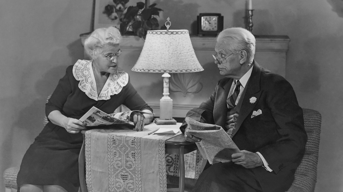 An old man reads a newspaper as his wife looks through a magazine circa 1940's. (Photo by FPG/Getty Images)