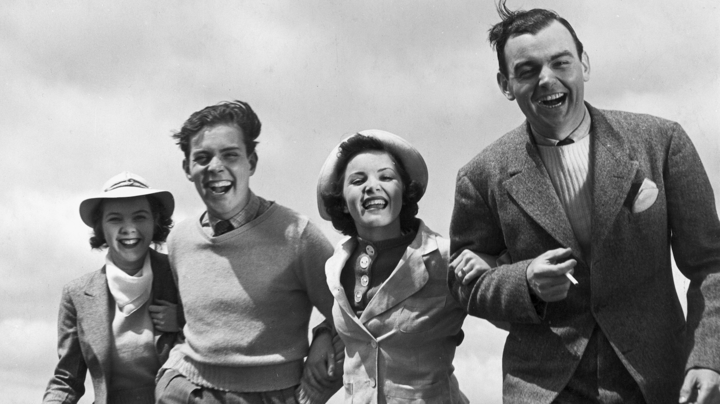 circa 1945: Two couples walk arm-in-arm outdoors, laughing. The wind blows the ladies' hats and the men's hair. (Photo by Hulton Archive/Getty Images)