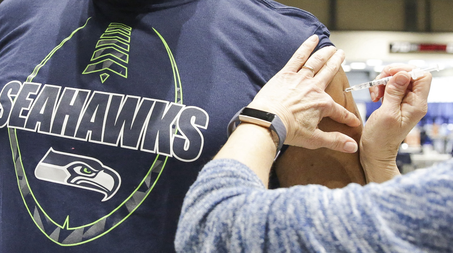 Cleveland Hughes wears Seahawks gear as he gets the Pfizer Covid-19 vaccine from Andrea Barnett during opening day of the Community Vaccination Site, a collaboration between the City of Seattle, First & Goal Inc., and Swedish Health Services at the Lumen Field Event Center in Seattle, Washington on March 13, 2021. (Photo by Jason Redmond / AFP) (Photo by JASON REDMOND/AFP via Getty Images)