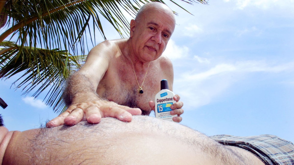 393787 01: Hector Ofunio applies suntan lotion to the back of his friend Leandro Munoz August 28, 2001 at the beach on Key Biscayne, Florida. (Photo by Joe Raedle/Getty Images)