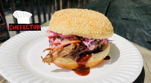 A pulled pork sandwich on a paper plate.