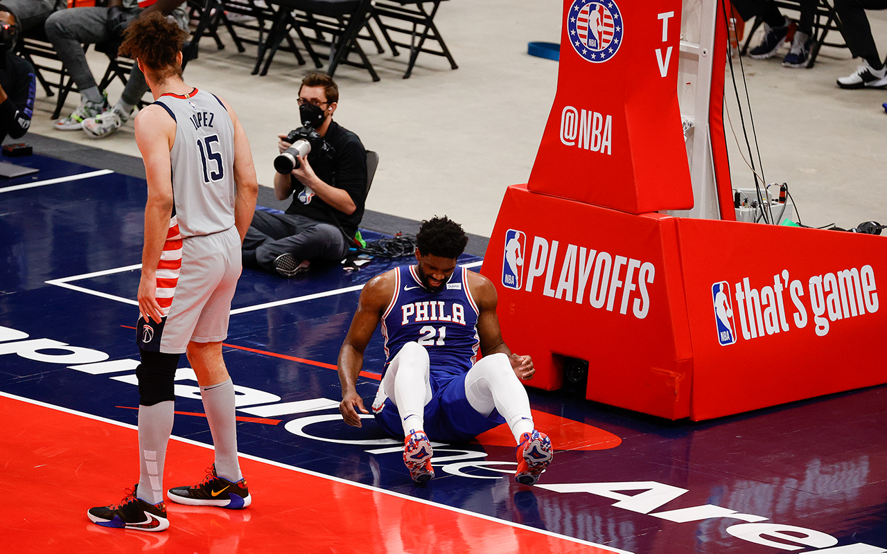 Joel Embiid lies on the court, clearly injured. Robin Lopez looks back at him.