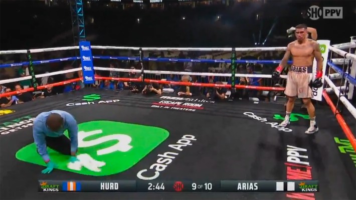 The ref wipes up a wet dollar sign logo in the center of the ring.