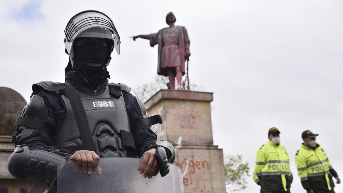 A statue of Christopher Columbus in Bogota, Colombia, defaced by protestors, is protected by armed police.