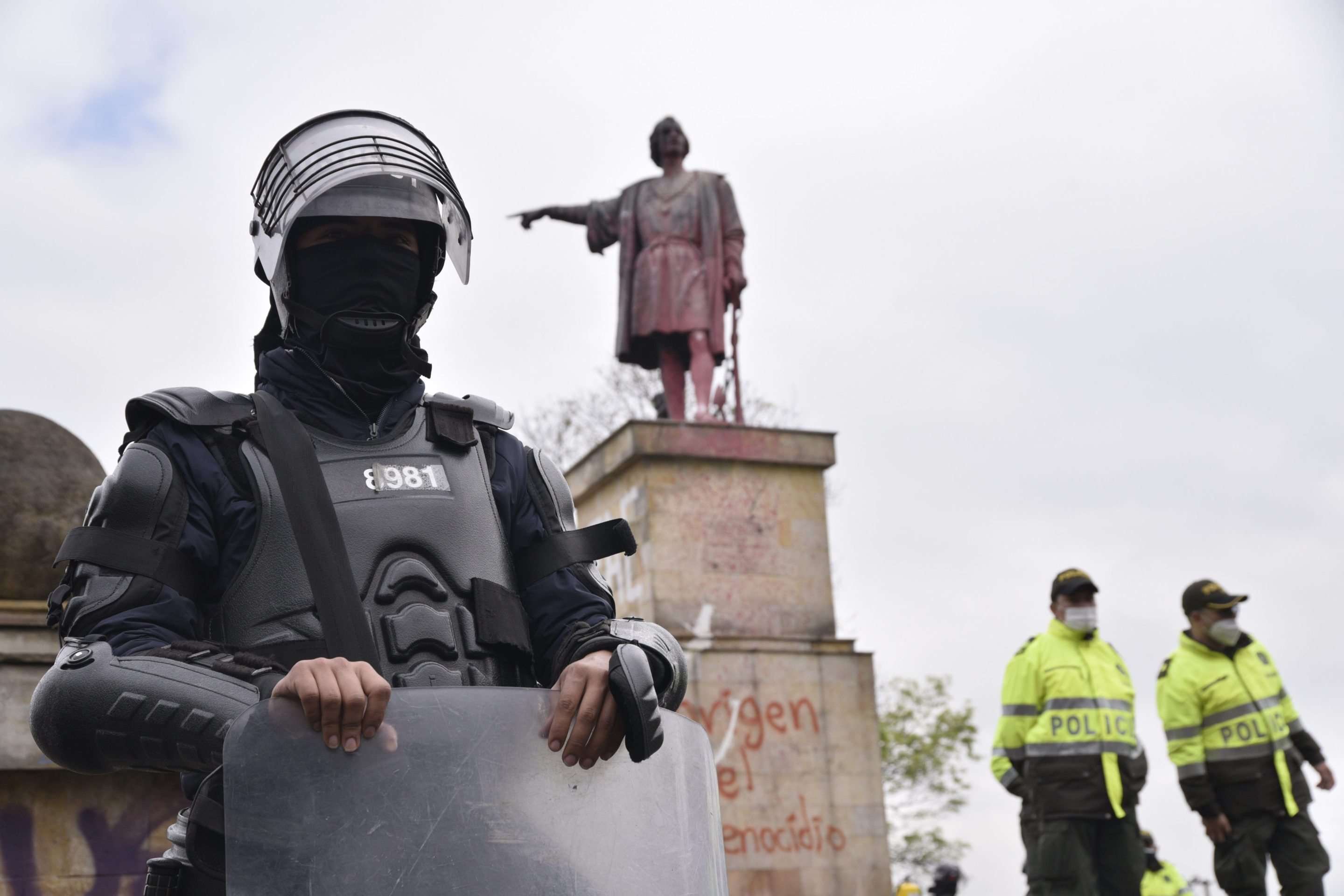 A statue of Christopher Columbus in Bogota, Colombia, defaced by protestors, is protected by armed police.
