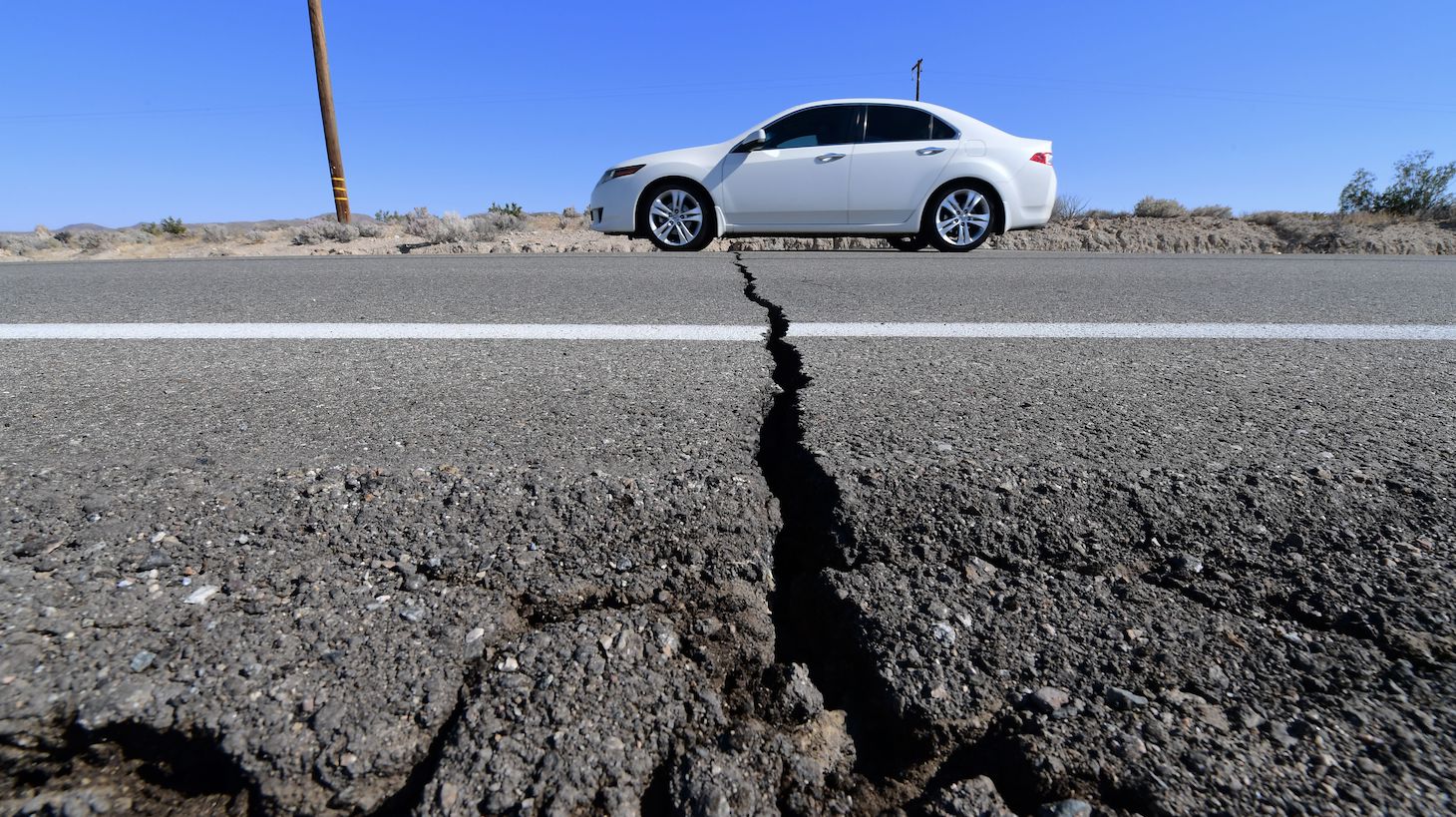 TOPSHOT - A car drives past a crack in the road on Highway 178, south of Trona, after a 6.4-magnitude earthquake hit in Ridgecrest, California, on July 4, 2019. - Southern California was rocked by a 6.4-magnitude earthquake Thursday morning, the US Geological Survey said, with authorities warning that the temblor, the largest in two decades, might not be the day's last. (Photo by FREDERIC J. BROWN / AFP) (Photo by FREDERIC J. BROWN/AFP via Getty Images)