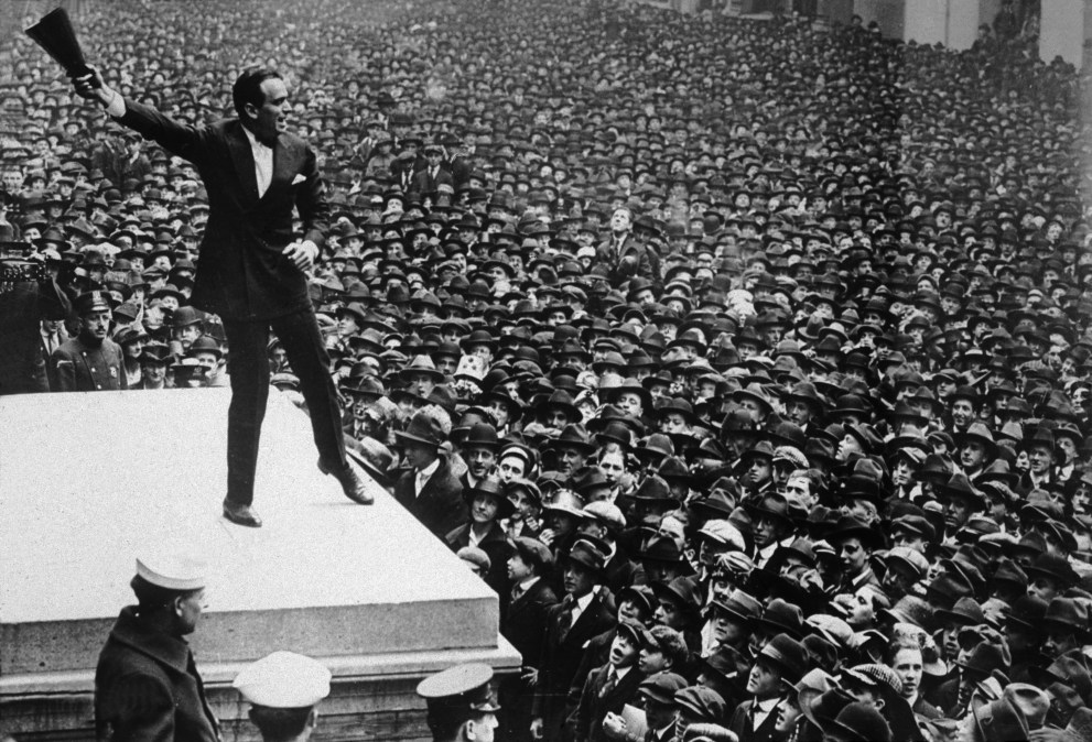 Full-length image of American actor Douglas Fairbanks Sr. waving a megaphone in the air while speaking from the Sub Treasury Building New York, to a sea of people, during a war bond rally, World War I.