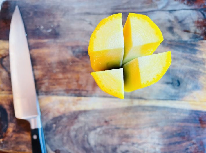 A yellow squash with the ends cut off, and sliced into quarters lengthwise