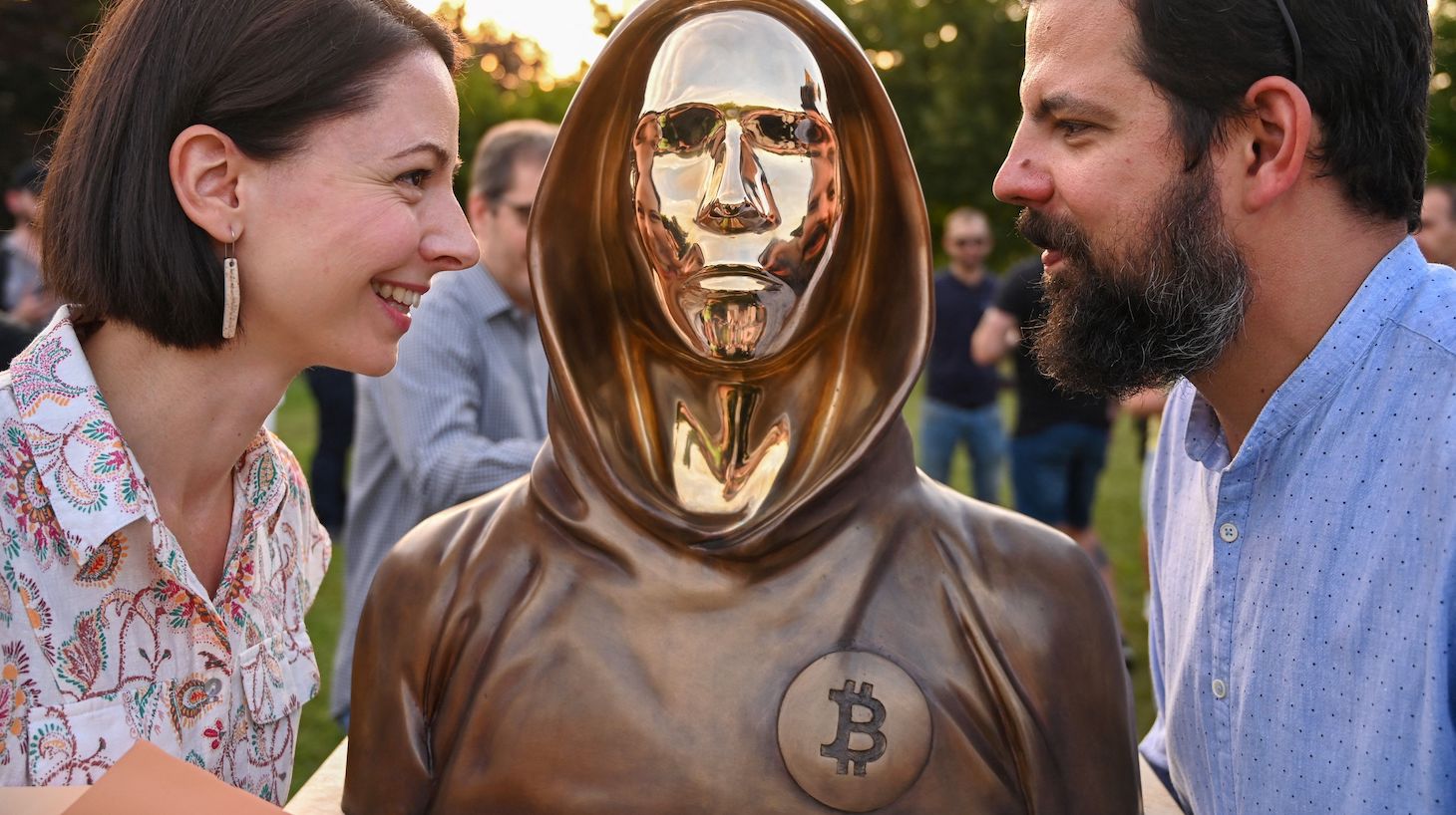 Hungarian sculptors and creators Reka Gergely (L) and Tamas Gilly (R) pose next to the statue of Satoshi Nakamoto, the mysterious inventor of the virtual currency bitcoin, after its unveiling at the Graphisoft Park in Budapest, on September 16, 2021. - Hungarian bitcoin enthusiasts unveiled a statue on September 16 in Budapest that they say is the first in the world to honour Satoshi Nakamoto, the mysterious inventor of the virtual currency. The bronze life-size sculpture depicts a hooded figure with stylised facial features, alluding to Nakamoto, a pseudonym credited as bitcoin's founder, but whose identity remains unknown. (Photo by ATTILA KISBENEDEK / AFP) (Photo by ATTILA KISBENEDEK/AFP via Getty Images)