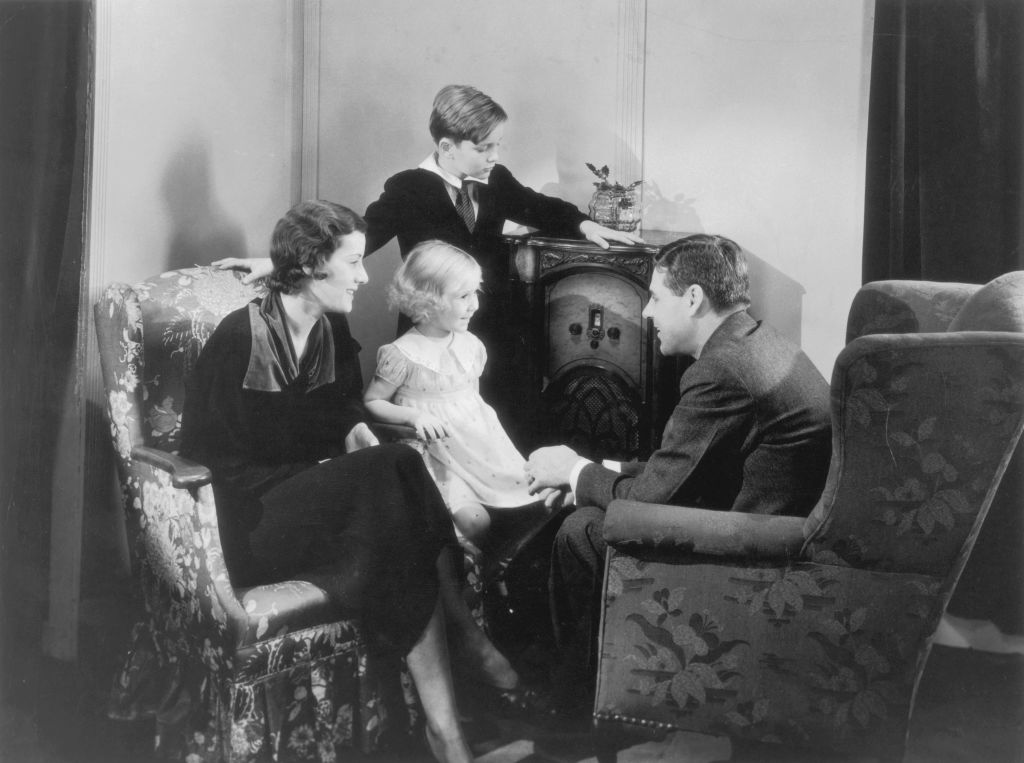 an old-timey family sitting around the radio