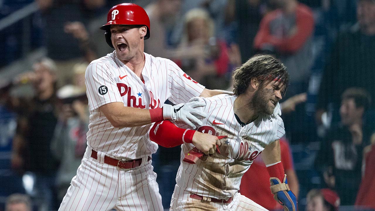 Bryce Harper looks kinda angry when celebrating, while Andrew Knapp hugs him from behind. They're clearly at home plate, and fans behind them are excited