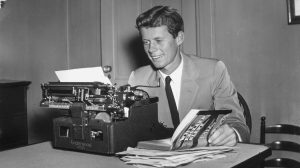 A young John F. Kennedy sits at a typewriter