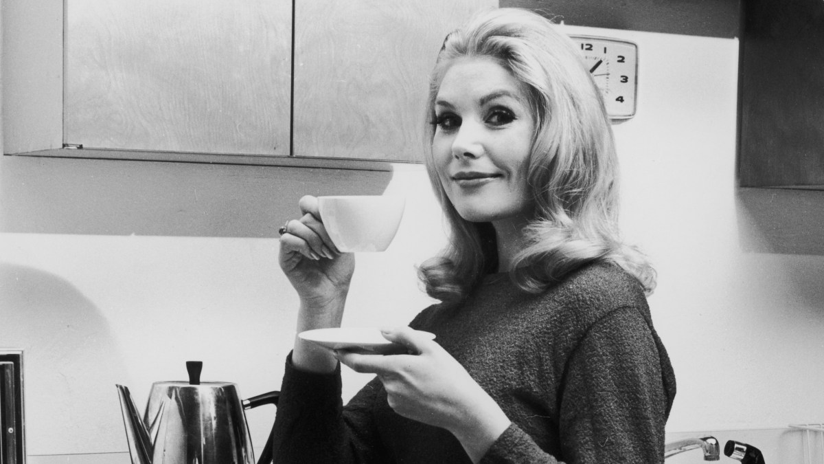 circa 1965: A woman lifts a cup of coffee off a saucer in a kitchen. (Photo by Leo Vals/Hulton Archive/Getty Images)