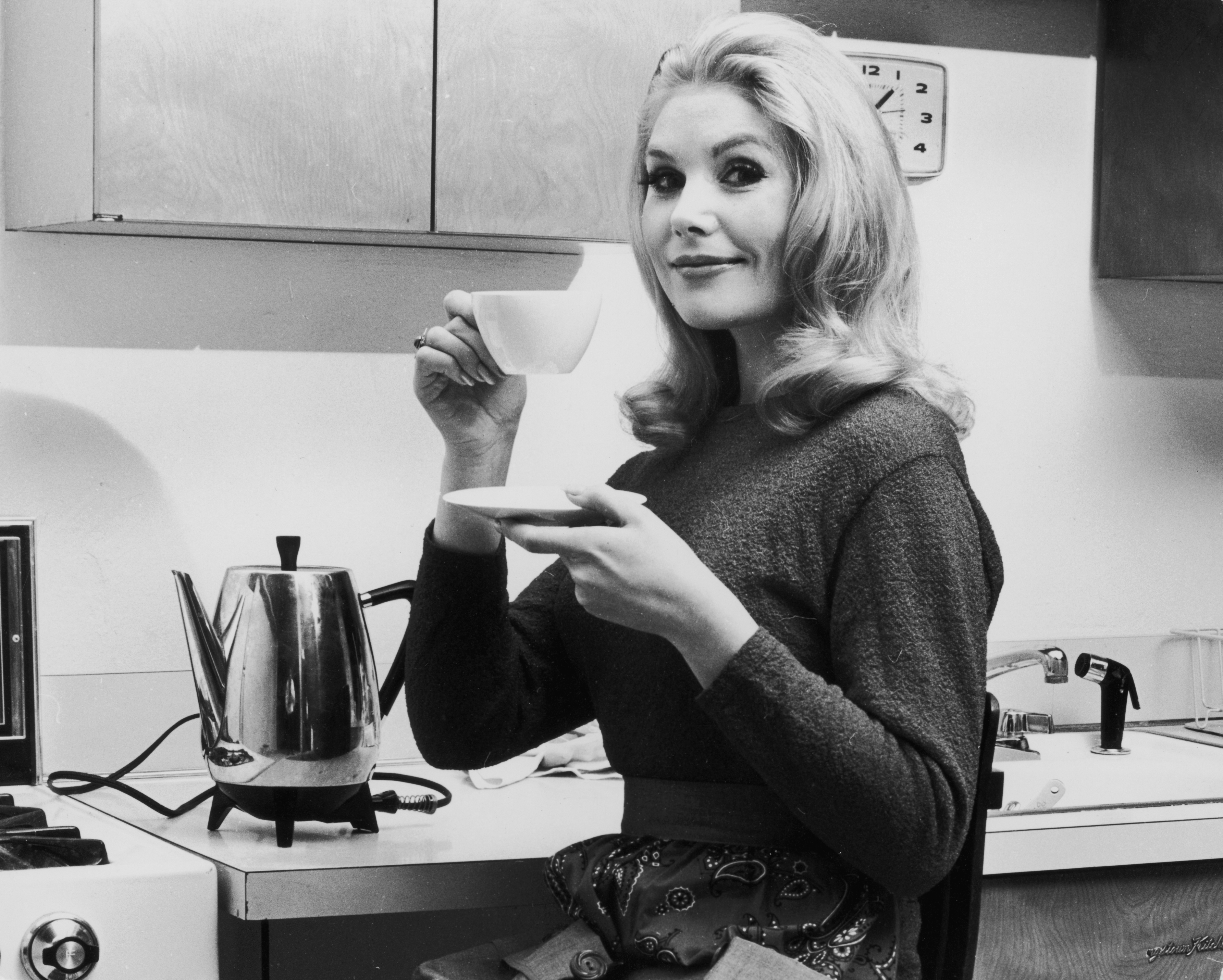 circa 1965: A woman lifts a cup of coffee off a saucer in a kitchen. (Photo by Leo Vals/Hulton Archive/Getty Images)