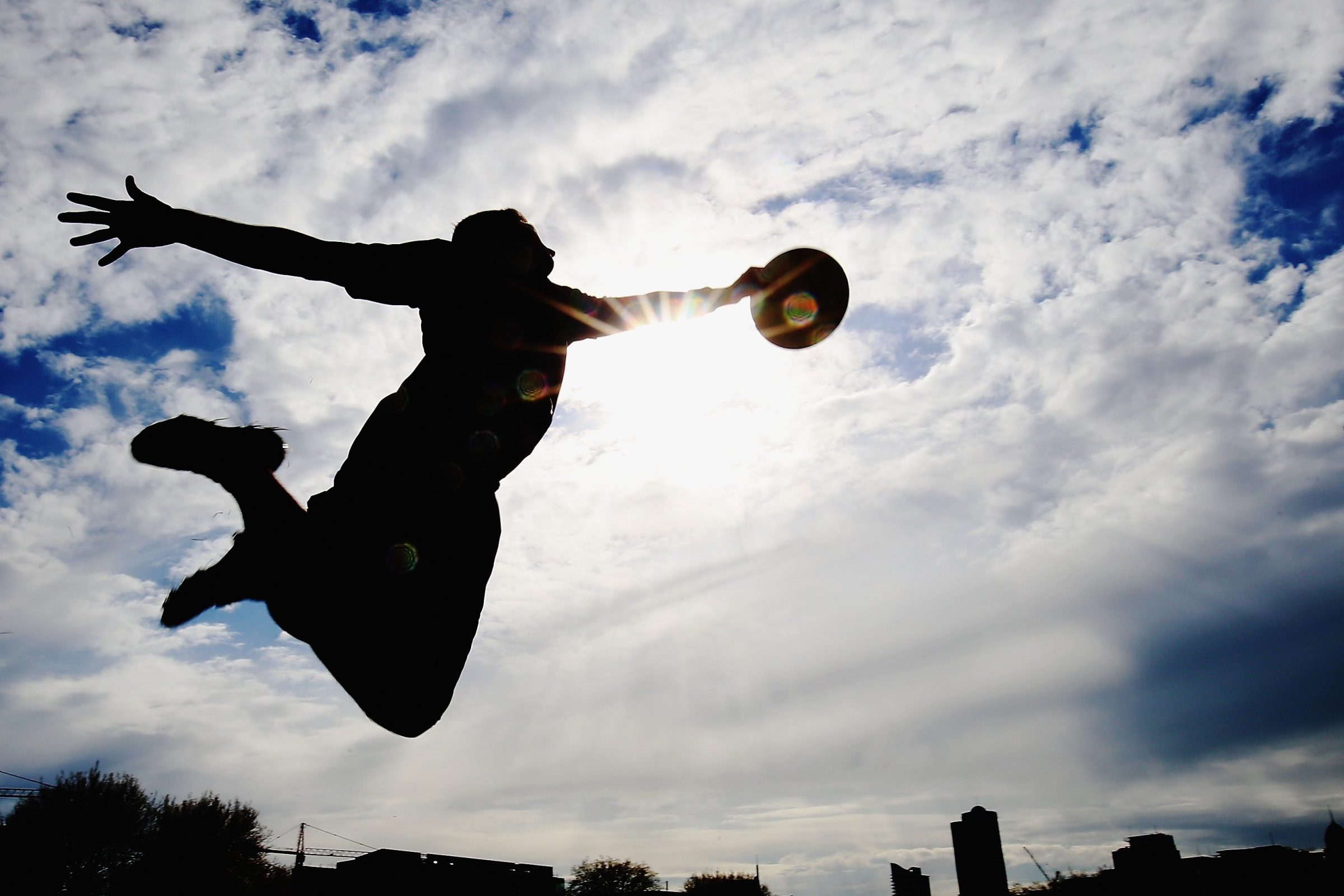 An ultimate frisbee player leaps to make a catch, silhouetted against the sun