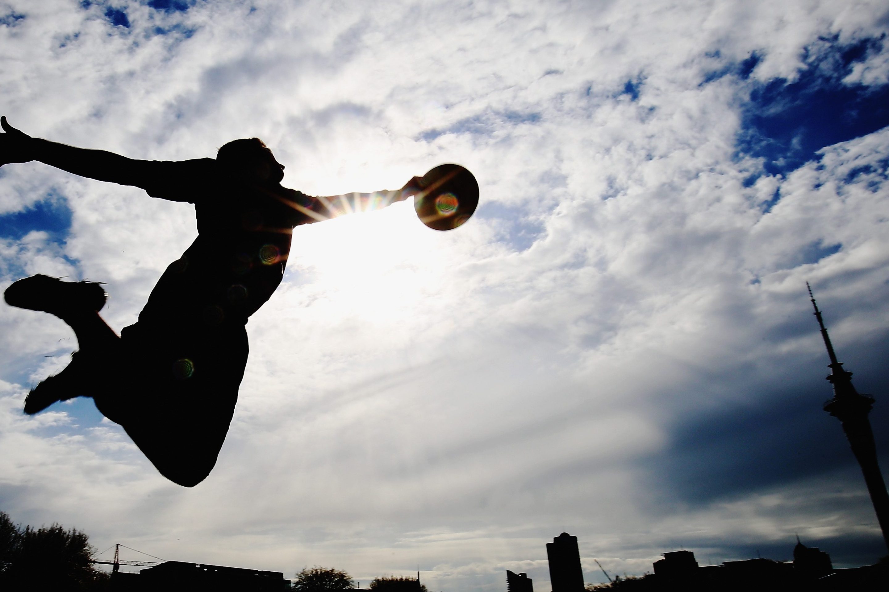 An ultimate frisbee player leaps to make a catch, silhouetted against the sun