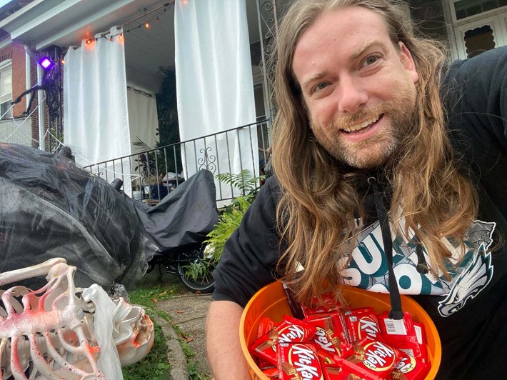 Dan McQuade *ooh he's so handsome* wearing an Eagles Super Bowl shirt next to a skeleton outfit holding a bowl of big bars