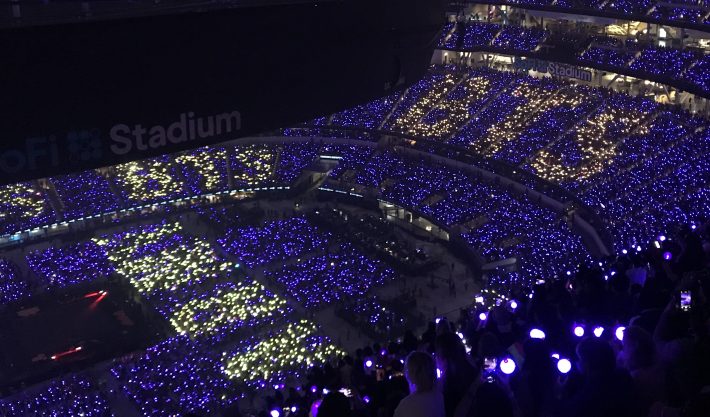 A photo showing lightsticks at a BTS concert. They are all illuminated to spell out the name of the band, BTS, and the name of their fanbase, ARMY.