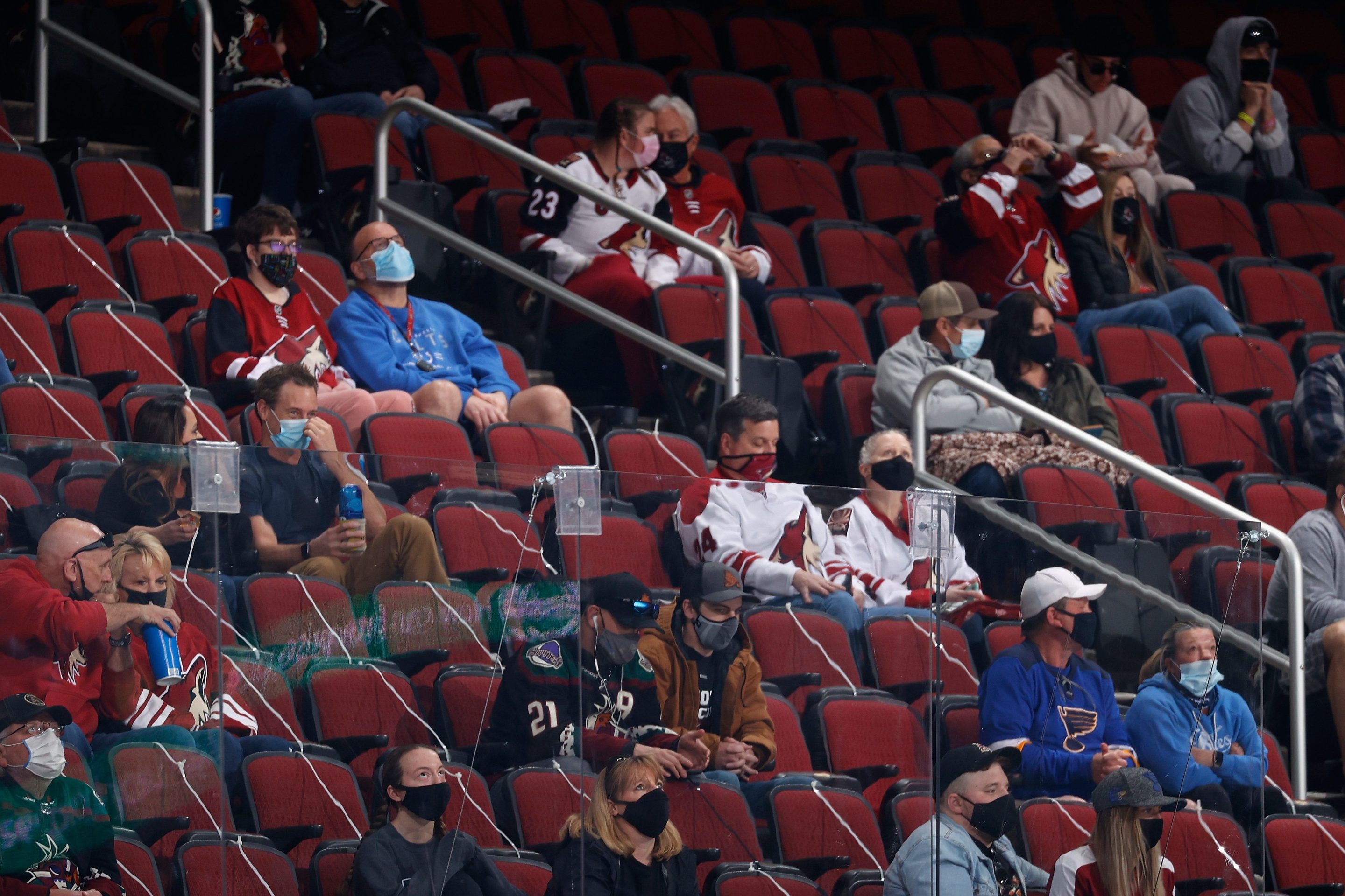 Fans watch from behind an extra sheet of plexy-glass, designed for greater protection, during the first period of the NHL game between the St. Louis Blues and the Arizona Coyotes at Gila River Arena on February 15, 2021 in Glendale, Arizona. The stands are mostly empty.
