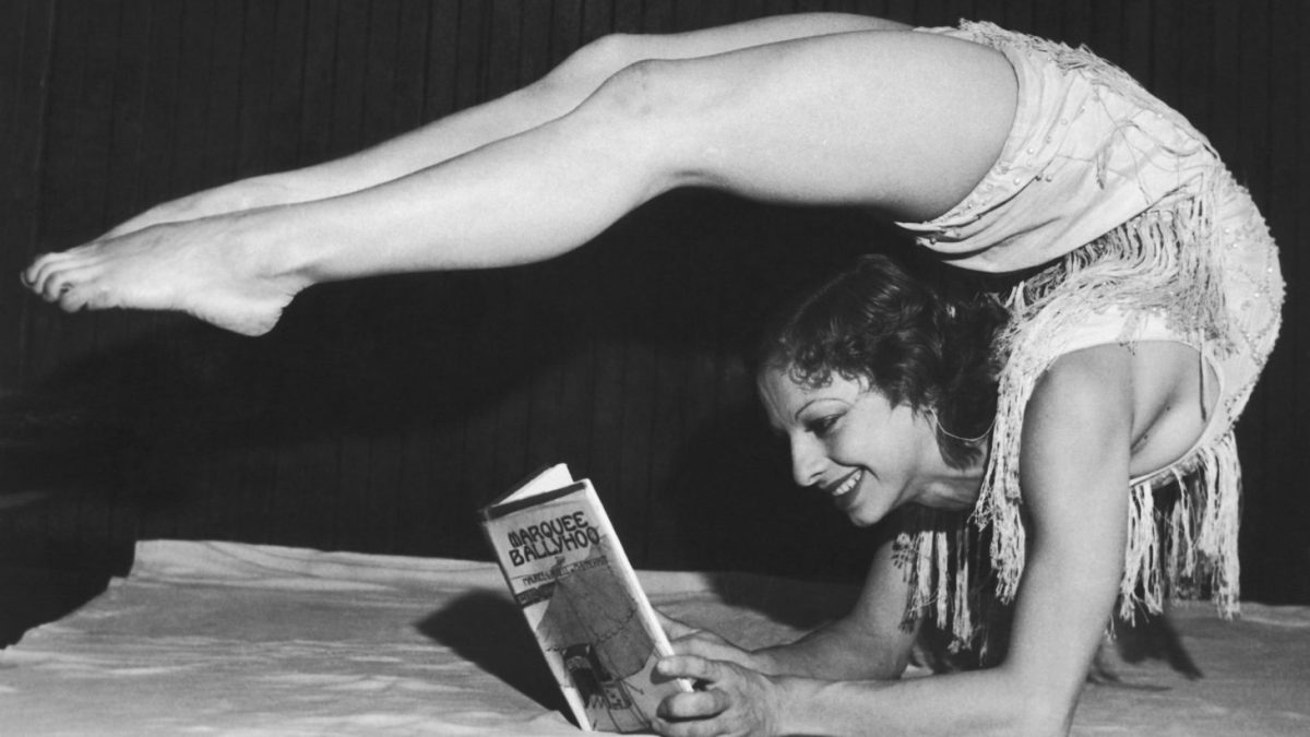 Dancer Gertrude Fisher laying with her legs bent over her head to read her husbands latest novel 'Marquee Ballyhoo', 1932.
