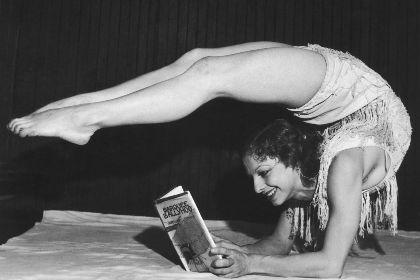 Dancer Gertrude Fisher laying with her legs bent over her head to read her husbands latest novel 'Marquee Ballyhoo', 1932.