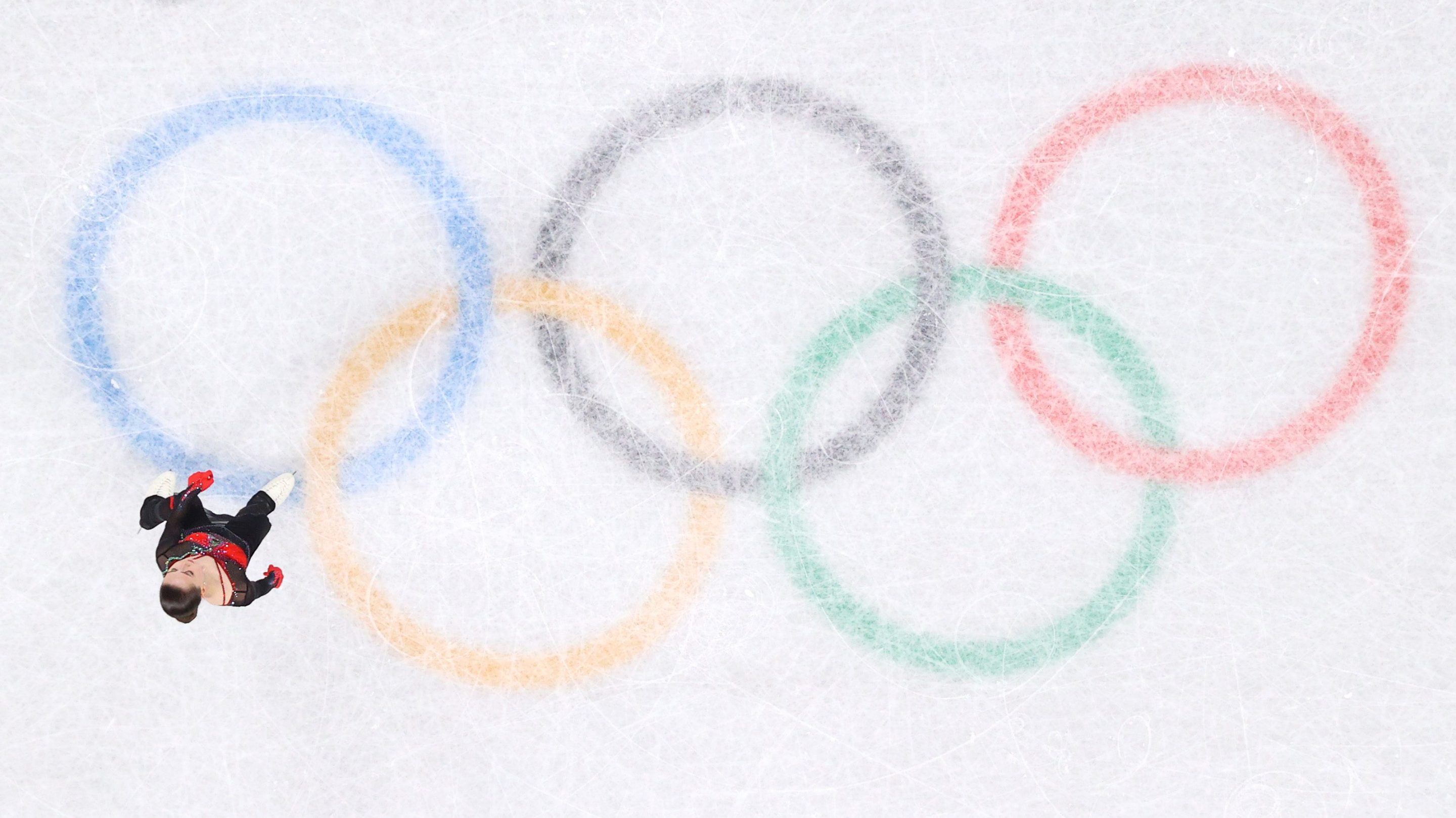 Kamila Valieva of Team ROC reacts after skating during the Women Single Skating Free Skating on day thirteen of the Beijing 2022 Winter Olympic Games at Capital Indoor Stadium on February 17, 2022 in Beijing, China. She is standing on center ice, looking very small, and all five Olympic rings on the ice are visible.