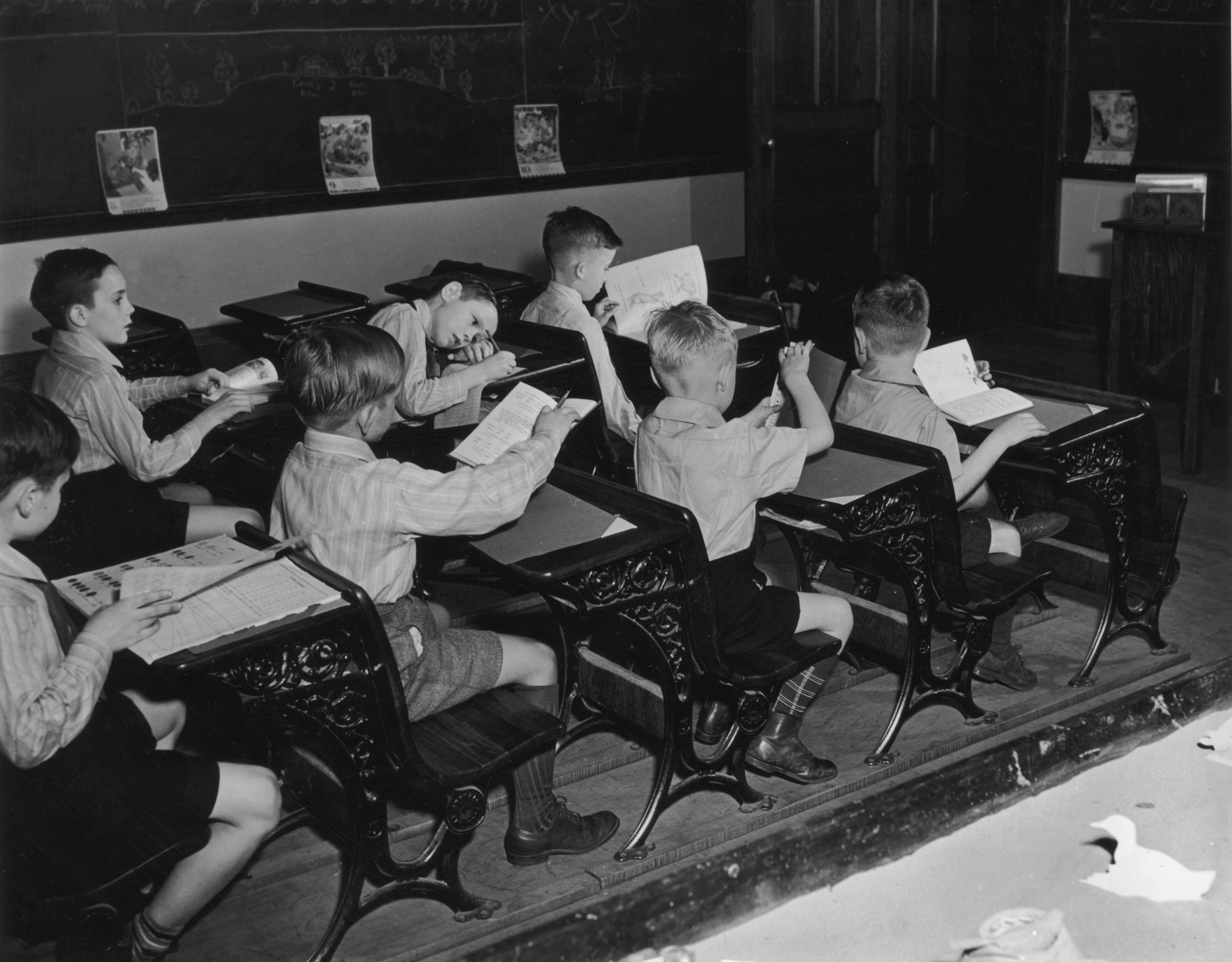 Students of a boy's school read and write while sitting at their desks in a classroom, Boden, Georgia. They wear shirts and shorts.
