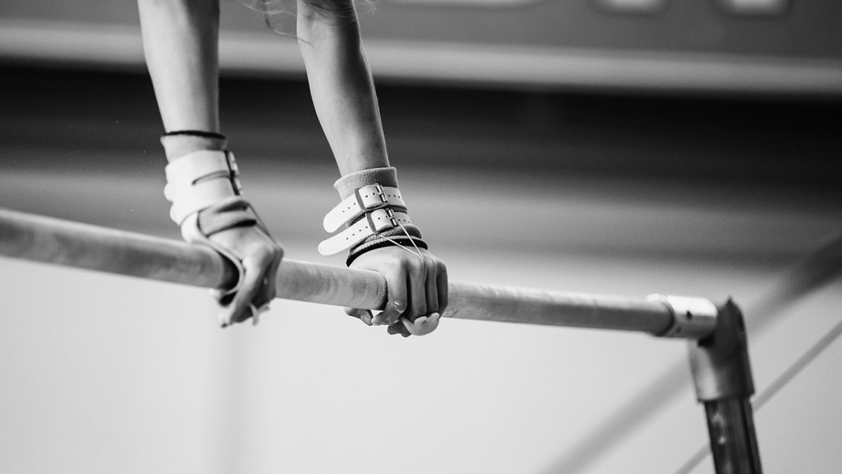 A photo of a pair of hands atop the uneven bars. They are griping the bars, as gymnasts do,