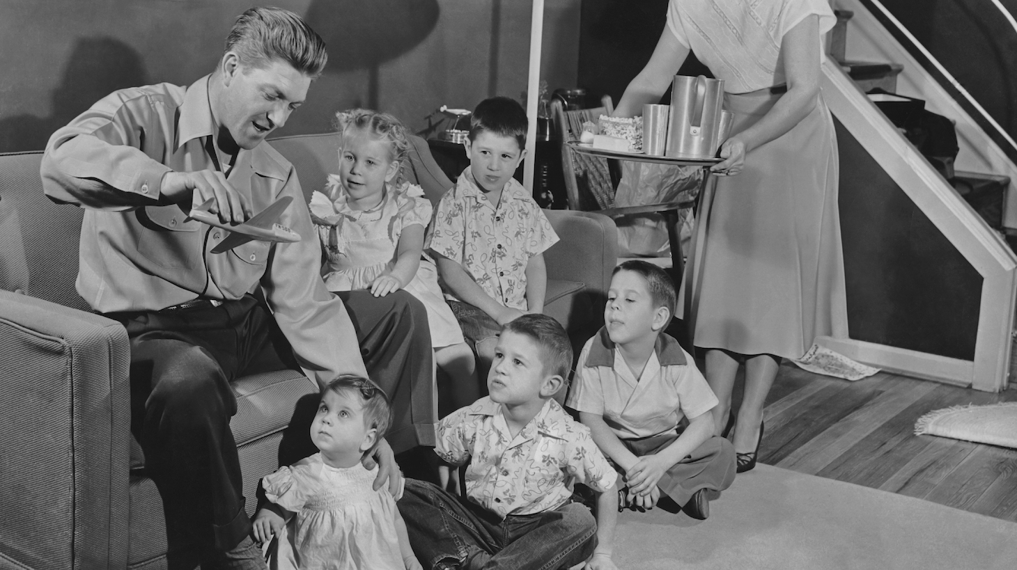 Father entertains five children with a toy airplane as mother carries in a tray of food circa 1950. (Photo by FPG/Getty Images)
