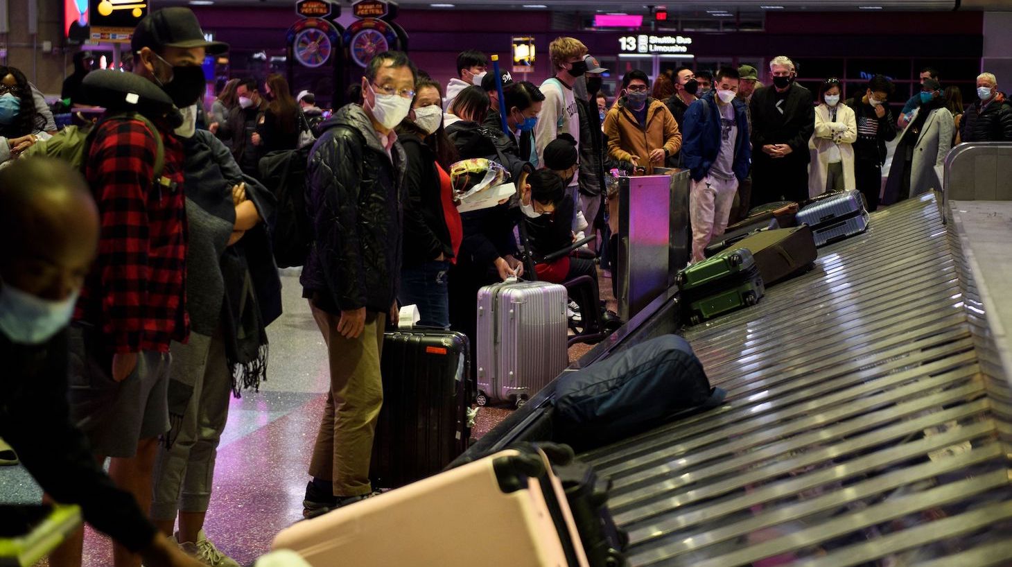 Airline passengers wearing face masks wait to collect bags from a baggage carousel at the Harry Reid International Airport (LAS) on January 2, 2022 in Las Vegas, California. - Americans returning home from holiday travel had to battle another day of airport chaos on January 2, with more than 2,000 flights cancelled due to bad weather or airline staffing woes sparked by a surge in Covid cases. (Photo by Patrick T. FALLON / AFP) (Photo by PATRICK T. FALLON/AFP via Getty Images)