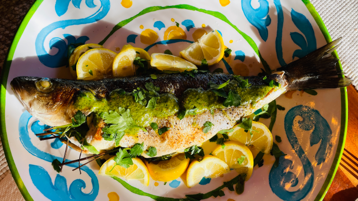 A roasted bronzino with salsa verde and lemon wedges